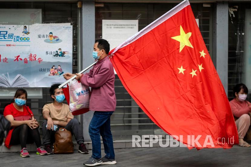 Seorang pria mengenakan masker saat berjalan membawa bendera Cina di Guangzhou, Guangdong, Cina, Selasa (28/4). 