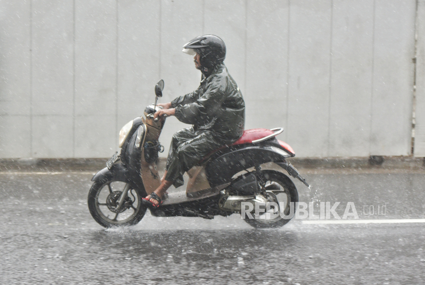 seorang pria mengendarai motor saat cuaca hujan 