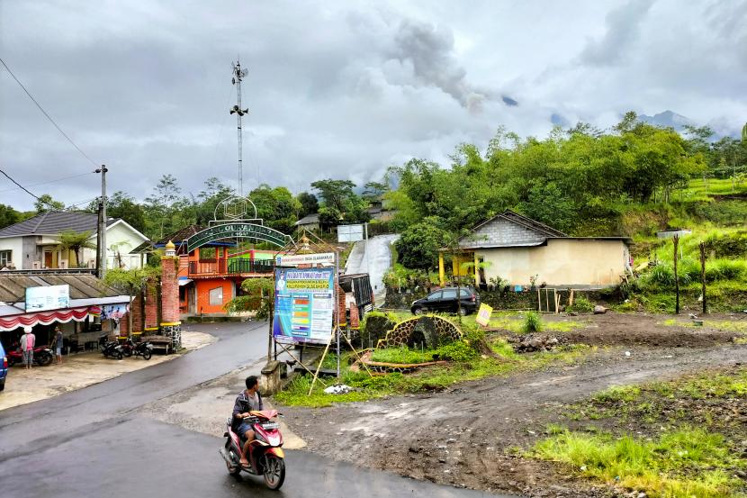 Seorang pria mengendarai sepeda motor melewati jalan dengan Gunung Merapi yang diselimuti kabut di latar belakang, terlihat dari desa Cangkringan di Sleman, Yogyakarta, Kamis, 10 Maret 2022. 