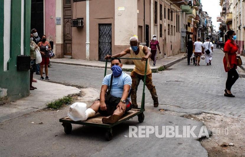 Seorang pria menggunakan masker didorong menggunakan troli akibat cedera pada kakinya di Havana, Kuba, Rabu (13/5). Pemerintah Kuba mewajibkan penggunaan masker  bagi siapa saja yang beraktivitas di luar rumah di tengah pandemi COVID-19. 