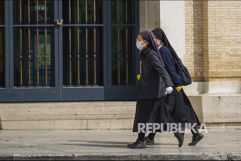 Dua orang biarawati menggunakan masker wajah berjalan di lingkungan di Roma Italia, Ahad (29/3). Italia mempersiapkan lima poin rencana saat kembali membuka bisnis secara bertahap 