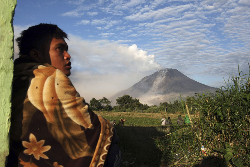  Seorang pria menyaksikan Gunung Sinabung menyemburkan debu vulkanik, di Desa Perteguhen, Karo, Sumut, Senin (6/1).    (AP/Binsar Bakkara)