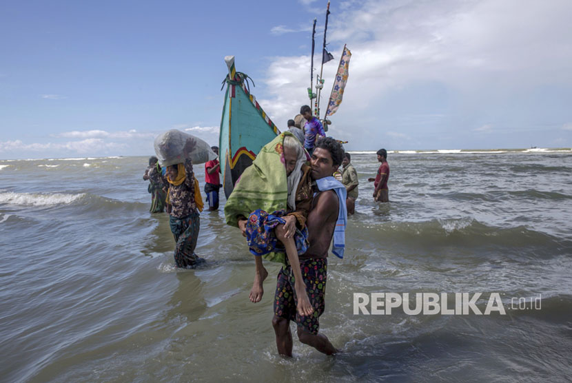 Seorang pria Muslim Rohingya berjalan ke pantai yang membawa seorang wanita tua setelah mereka tiba di sebuah kapal dari Myanmar ke Bangladesh di Shah Porir Dwip, Bangladesh, Kamis, (14/9).