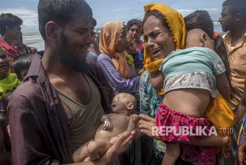  Seorang pria Muslim Rohingya Naseer Ud Din memegang anak laki-lakinya, Abdul Masood, yang tenggelam saat kapal yang mereka tumpangi terbalik sebelum mencapai pantai, saat istrinya Hanida Begum menangis saat mencapai pantai Teluk Benggala di Shah Porir Dwip, Bangladesh, Kamis, (14/9).