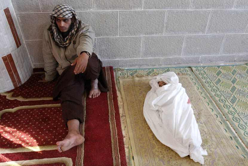  Seorang pria Palestina duduk di samping jenazah anaknya yang berusia satu setengah tahun di Kamp Pengungsi Bureij,Gaza, Ahada (18/11). (AP Photo/Adel Hana)