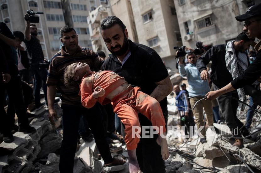 Seorang pria Palestina membawa seorang anak yang meninggal  dibawa dari puing-puing bangunan tempat tinggal yang hancur setelah serangan udara Israel di Kota Gaza, Ahad (16/5). Kemenlu Palestina: Israel Sengaja Bunuh 44 Anak Palestina selama 2022