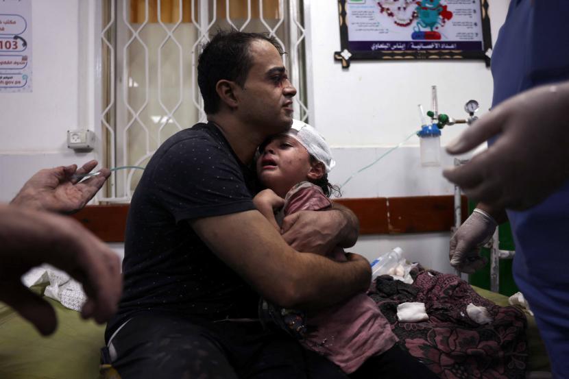Seorang pria Palestina menggendong seorang anak yang terluka di rumah sakit Najjar menyusul serangan udara Israel terhadap sebuah rumah di Rafah, di Jalur Gaza selatan.