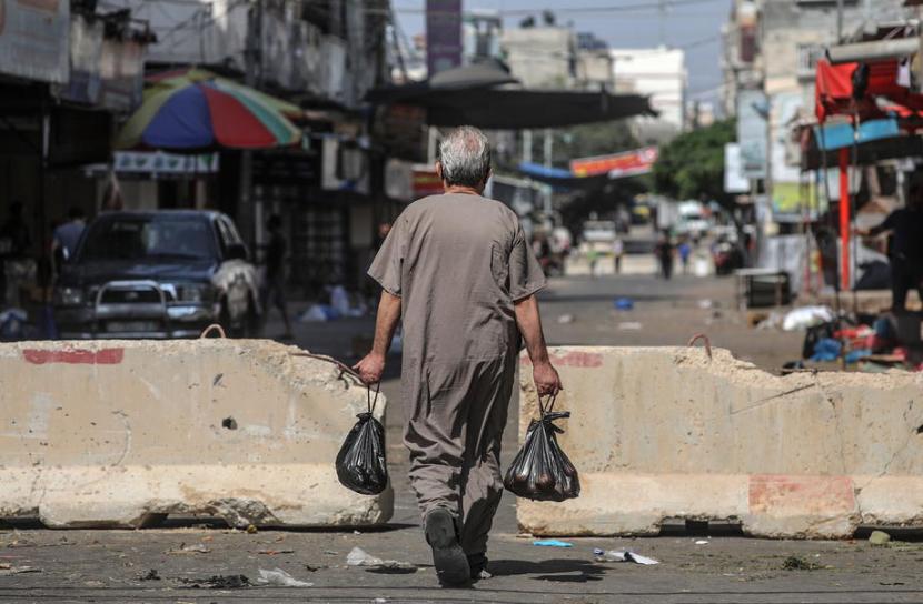  Seorang pria Palestina yang membawa barang belanjaan untuk keluarganya tampak menyeberang penghalang beton yang digunakan untuk mengisolasi jalan yang menuju antara Gaza dan Jalur Gaza utara di tengah pandemi Covid-19 yang sedang berlangsung di Kota Gaza, Jalur Gaza, Sabtu, (29/8).