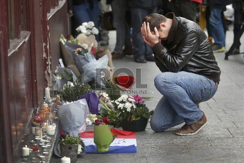 Seorang pria termenung seusai meletakkan karangan di luar restoran Le Carillon, Paris, Sabtu (14/11). REUTERS / Christian Hartman