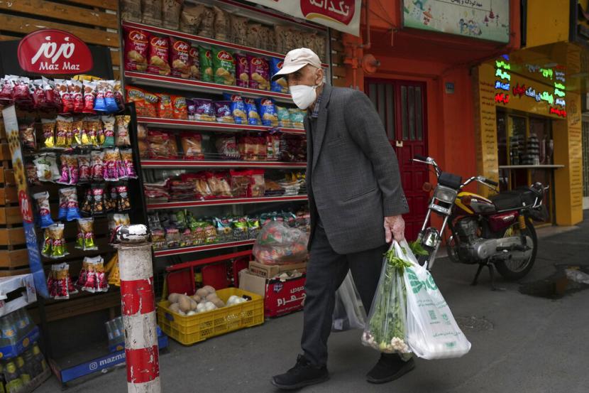 Seorang pria tua membawa belanjaannya di depan sebuah toko kelontong di Teheran, Iran, Rabu, 11 Mei 2022. Iran tiba-tiba menaikkan harga sebanyak 300% untuk berbagai bahan pokok seperti minyak goreng, ayam, telur, dan susu pada Kamis.