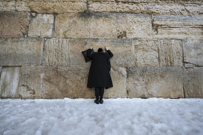 Seorang pria Yahudi ultra-Ortodoks berdiri di atas salju sambil berdoa di Tembok Barat, situs paling suci di mana orang-orang Yahudi dapat berdoa di kota tua Yerusalem, Kamis, 27 Januari 2022. 