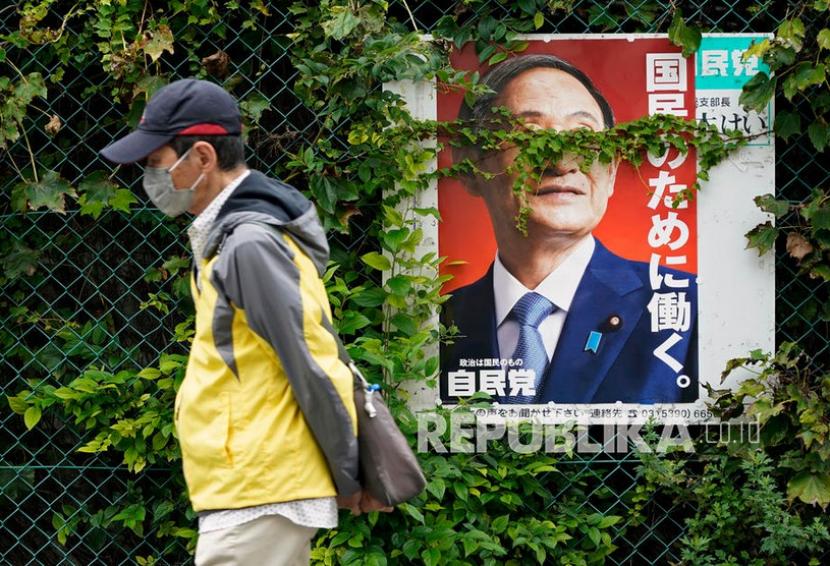 Seorang pria yang mengenakan masker berjalan melewati poster yang ditutupi dengan vegetasi yang menunjukkan Perdana Menteri Jepang Yoshihide Suga yang akan keluar di Tokyo, Jepang, 17 September 2021. Tiga Negara Ini Alami Lonjakan Tinggi Covid-19