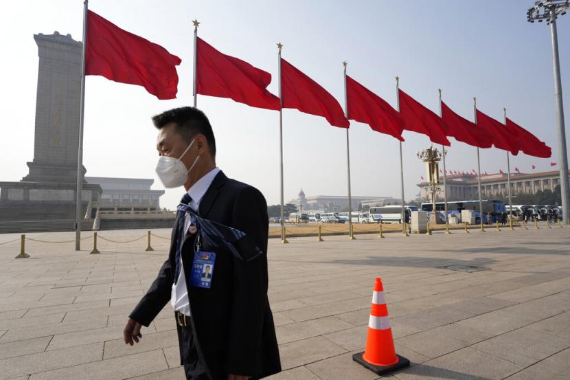 Seorang pria yang mengenakan topeng berjalan di dekat bendera merah di Tiananmen Square pada malam sesi pembukaan pertemuan tahunan Kongres Rakyat Nasional Tiongkok (NPC) di Beijing, Sabtu, 4 Maret 2023.