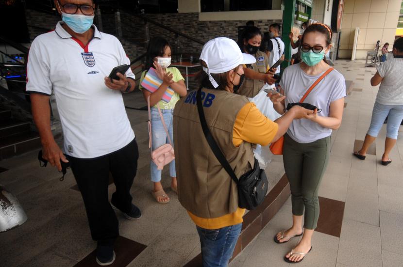 Seorang relawan Badan Nasional Penanggulangan Bencana (BNPB) membagiakan masker kepada pengunjung salah satu pusat perbelanjaan di Manado, Sulawesi Utara, Sabtu (9/10/2021). Pembagian paket masker, cairan pensanitasi tangan serta sabun cuci tangan kepada masyarakat dilakukan sebagai upaya mengedukasi dan membangun kesadaran masyarakat atas kebersihan diri dalam masa pendemi, serta sebagai mitigasi penyebaran Covid-19. Positif Covid-19 di Sangihe Bertambah Empat Kasus Menjadi 11 Orang