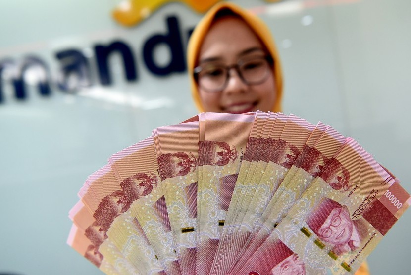 Seorang teller Bank Mandiri menunjukkan uang pecahan Rp100.000 di Plasa Mandiri, Jakarta, Senin (8/7/2019).