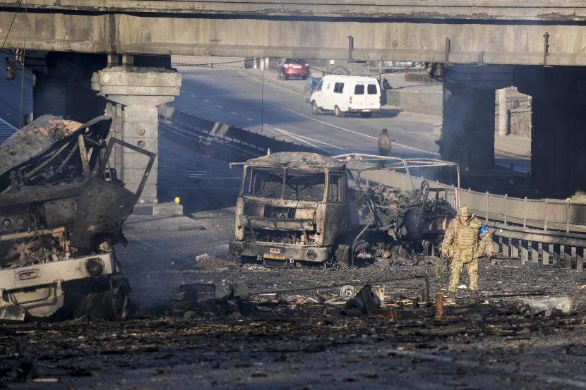 Seorang tentara Ukraina berjalan melewati puing-puing truk militer yang terbakar, di sebuah jalan di Kyiv, Ukraina, Sabtu, 26 Februari 2022. Pasukan Rusia menyerbu ke arah ibu kota Ukraina Sabtu, dan pertempuran jalanan pecah saat pejabat kota mendesak penduduk untuk berlindung.
