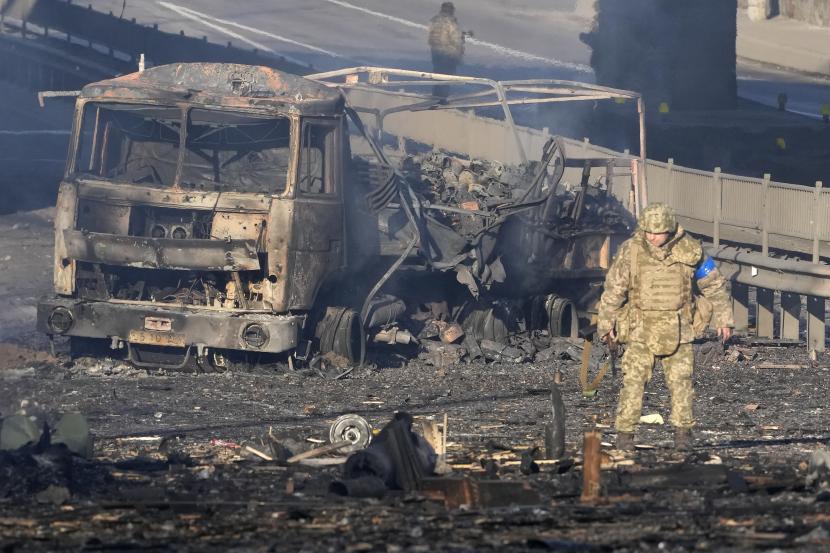 Seorang tentara Ukraina berjalan melewati puing-puing truk militer yang terbakar, di sebuah jalan di Kyiv, Ukraina, Sabtu, 26 Februari 2022. 