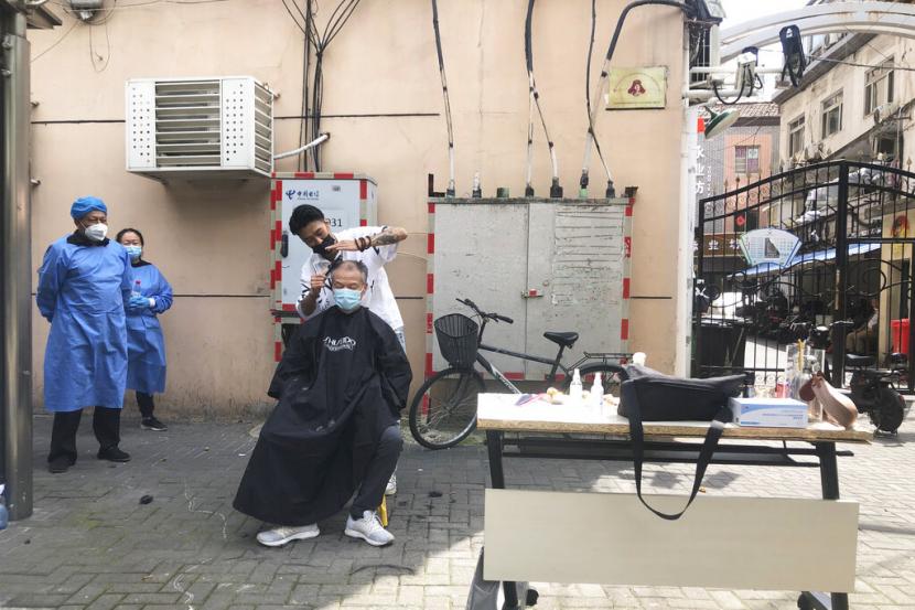 Seorang tukang cukur menawarkan potong rambut gratis untuk warga lanjut usia melayani pelanggan di Shanghai, China, Ahad, 22 Mei 2022. Beijing memperpanjang peraturan pembatasan sosial Covid-19 