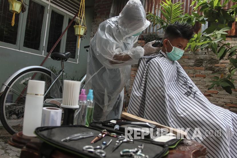 Dumai Diminta Segera Ajukan PSBB. Seorang tukang cukur menggunakan Alat Pelindung Diri (APD) ketika memotong rambut di halaman rumah pelanggan, di Pekanbaru, Riau, Kamis (9/4/2020). Sepinya pengunjung yang datang ke barbershop membuat pelaku usaha potong rambut menerima jasa panggilan cukur ke rumah dengan menggunakan pakaian pelindung untuk pencegahan penularan virus Corona (COVID-19).