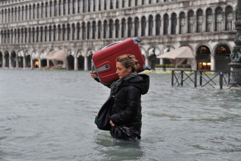 Seorang turis dengan mengangkat koper besar miliknya melintas di St Mark's Square, Venice, Italia, yang direndam banjir, Ahad (11/11). 