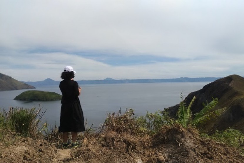 Seorang turis lokal memandangi keindahan Danau Toba dari atas bukit.