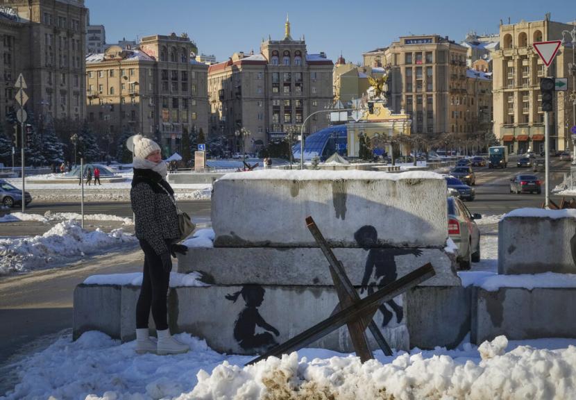 Seorang wanita berdiri di samping gambar dengan karya seni di balok beton yang dipasang untuk melindungi kota dari pasukan Rusia, di alun-alun utama di Kyiv, Ukraina, Kamis, 1 Desember 2022. Lukisan itu tampaknya dibuat oleh Seniman jalanan Inggris Banksy, yang mengonfirmasi hal ini di akun Instagram-nya.