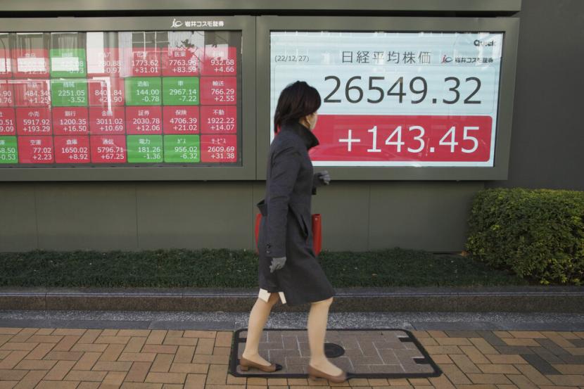  Seorang wanita berjalan melewati monitor yang menunjukkan indeks Nikkei 225 Jepang. ilustrasi