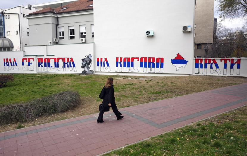 Seorang wanita berjalan melewati mural yang menggambarkan peta Kosovo yang dicat dengan warna bendera Serbia, bertuliskan: 