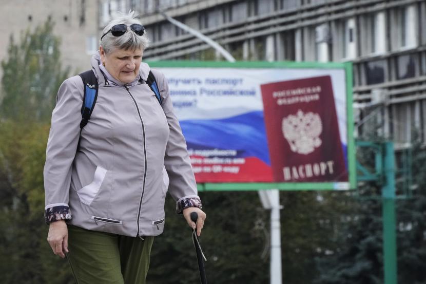 Seorang wanita berjalan melewati papan iklan bergambar paspor Rusia, sehari setelah pemungutan suara di empat wilayah Ukraina yang dikuasai Moskow pada referendum untuk menjadi bagian dari Rusia, di Luhansk, Republik Rakyat Luhansk yang dikendalikan oleh separatis yang didukung Rusia, Ukraina timur, Rabu, 11 September. 28, 2022. 