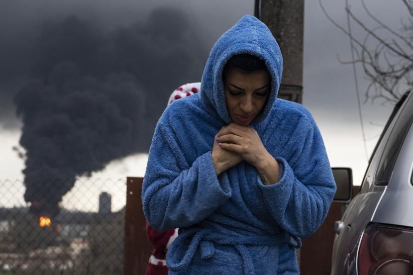 Seorang wanita berjalan saat asap mengepul di udara di latar belakang setelah penembakan di Odesa, Ukraina, Ahad, 3 April 2022. 