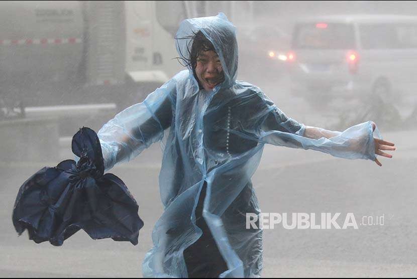 Seorang wanita berlari di antara terpaan hujan badai di China. Kementerian China perkirakan topan Hinnamnor akan menimbulkan kerusakan parah. Ilustrasi.
