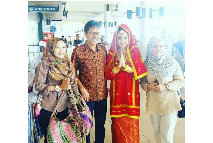 Seorang  wanita berpakaian adat memberikan selendang sarung dan anyaman khas minang kepada para wisatawan yang datang di Bandara Internasional Minangkabau.
