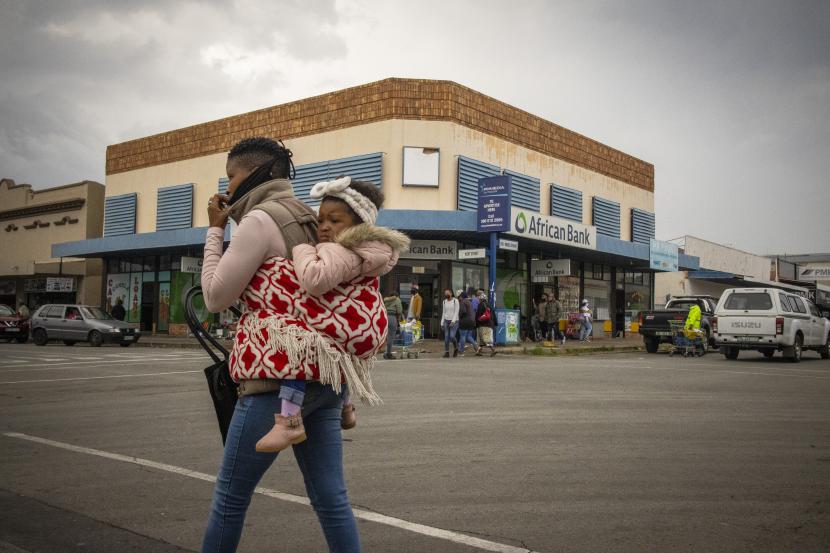 Seorang wanita bertopeng menggendong seorang anak berjalan melalui jalan-jalan di kota pedesaan Parys, Afrika Selatan, 26 November 2021. Departemen Kesehatan Afrika Selatan dan ilmuwan dari Network for Genomic Surveillance mengungkapkan rincian Covid-19 yang baru terdeteksi dan sangat bermutasi varian, B.1.1.529.