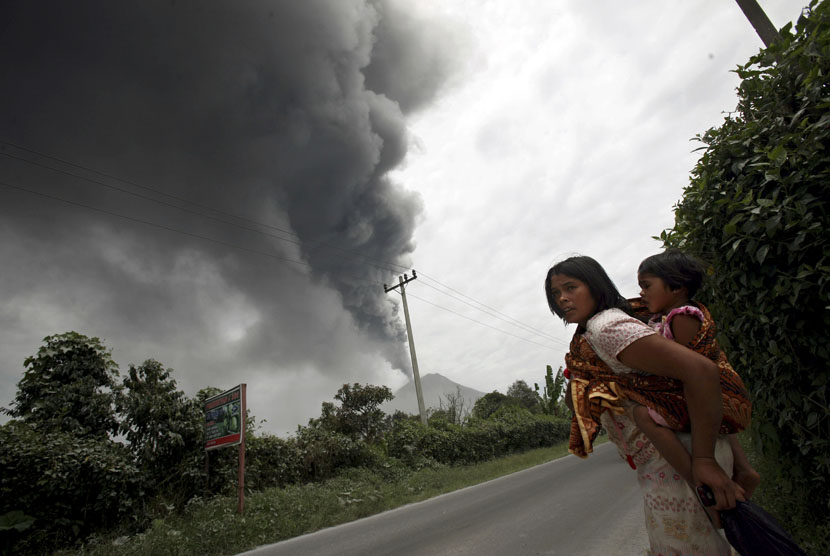  Seorang wanita dan putrinya meninggalkan rumah mereka saat Gunung Sinabung meletus di Karo, Sumatera Utara, Selasa, 17/9).  (AP/Binsar Bakkara)