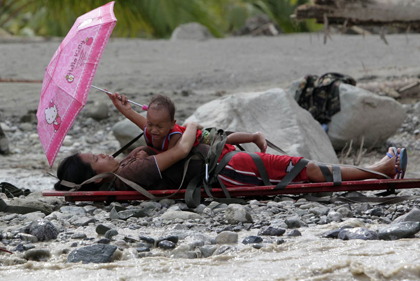   Seorang wanita hamil yang selamat dari banjir memegang anaknya diatas tandu sambil menunggu untuk dievakuasi di kota New Bataan,Filipina, Kamis (6/12). (Reuters/Erik De Castro)