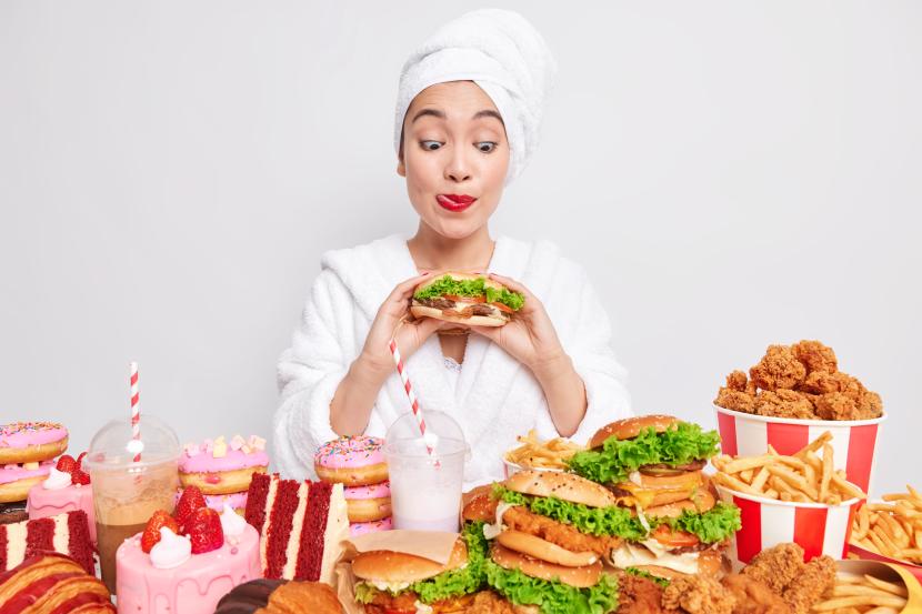 Seorang wanita makan berlebihan (ilustrasi). Hindari pula makanan olahan atau ultraproses yang mengandung banyak gula, garam, dan lemak agar kadar kolesterol terjaga.