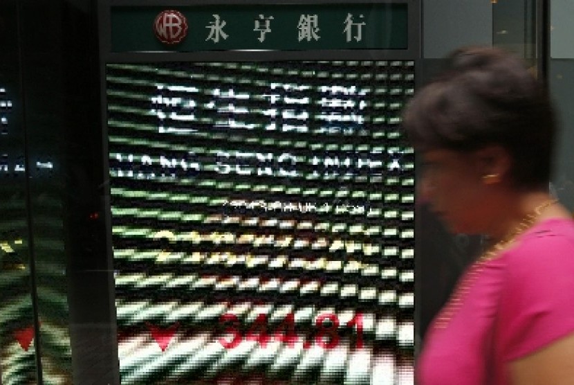 Seorang wanita melintas di depan papan elektronik yang menunjukan indeks saham Hong Kong