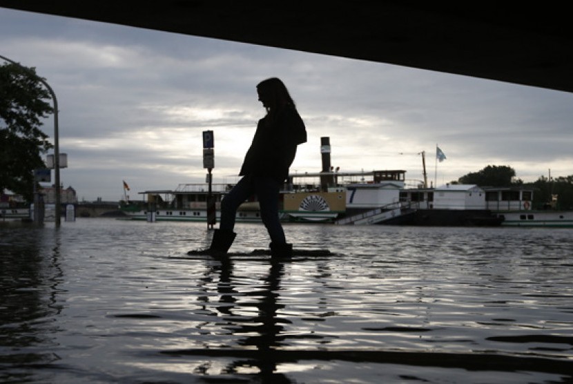  Seorang wanita memakai sepatu bot karet berjalan melintasi genangan air di bawah jembatan di Dresden, Jerman, Senin (3/6) waktu setempat.    (AP/Markus Schreiber)