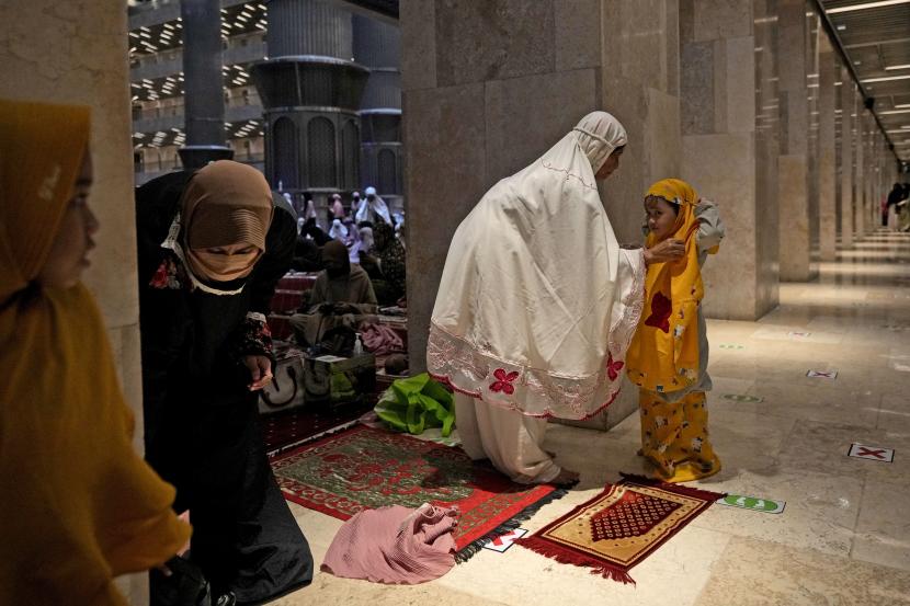 Seorang wanita membantu putrinya mengenakan jubah sholat sebelum memulai 