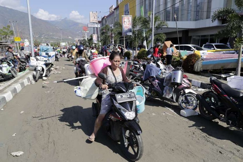 Seorang wanita membawa barang-barang yang diduga hasil jarahan di Palu, Sulteng, Ahad (30/9).