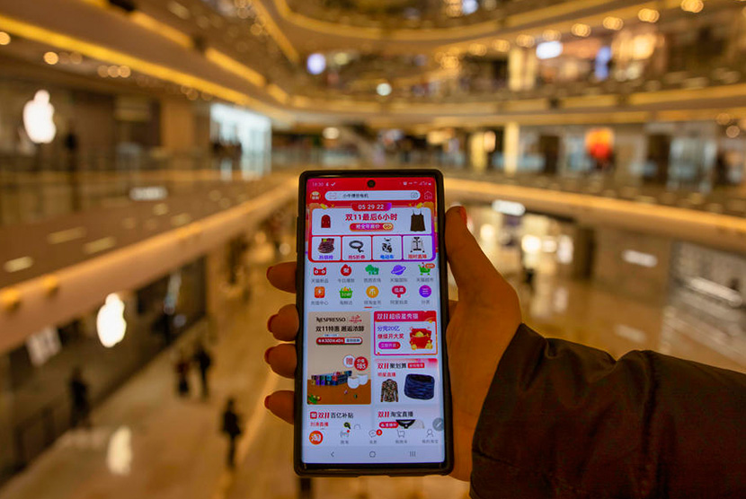 Seorang wanita memegang ponsel pintar dengan aplikasi belanja Taobao.