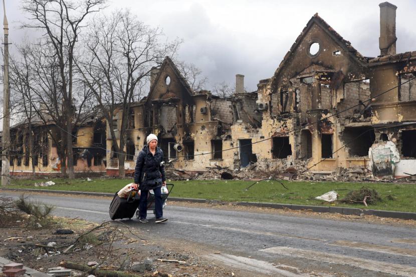 Seorang wanita menarik tasnya melewati rumah-rumah yang rusak selama pertempuran di Mariupol, di wilayah yang sekarang berada di bawah kendali Pemerintah Republik Rakyat Donetsk, timur di Mariupol, Ukraina, Jumat, 8 April 2022.