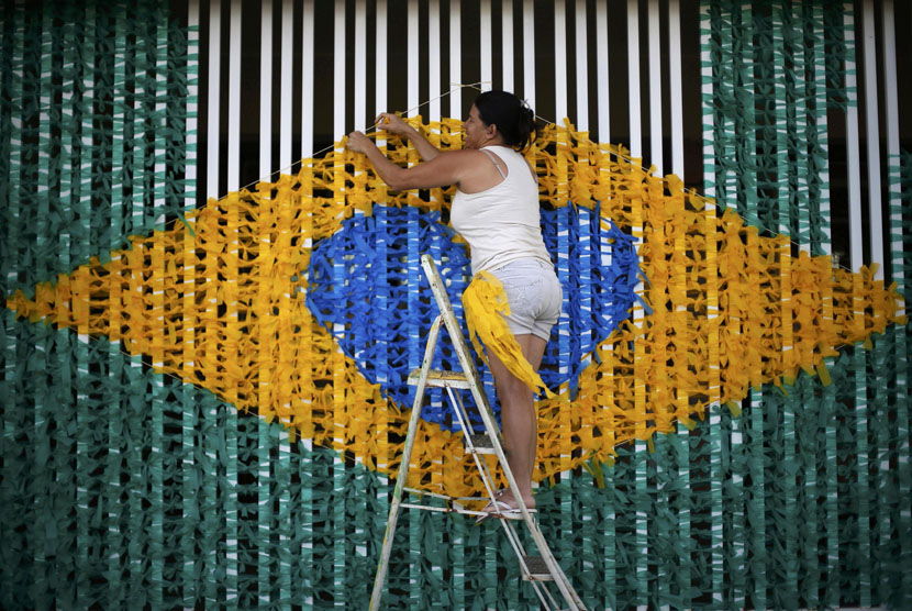 Seorang wanita mengikati pita membentuk pola bendera nasional Brasil di jalanan yang dihiasi warga setempat untuk menyambut Piala Dunia 2014. 