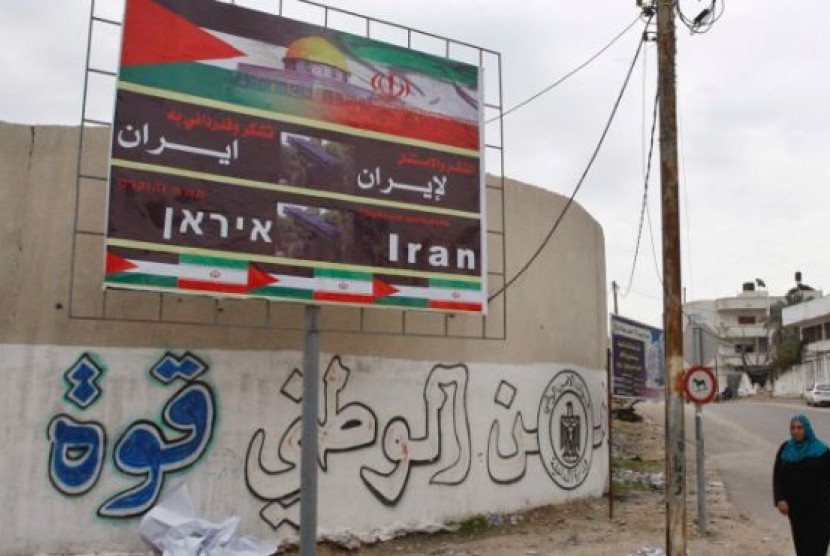 Seorang wanita Palestina berjalan melewati baliho yang bertuliskan 'Terima Kasih Iran' di Kota Gaza, Palestina, Selasa (27/11)