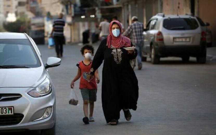 Seorang wanita Palestina membawa sepiring makanan saat dia berjalan bersama anaknya, keduanya mengenakan masker, di Kota Gaza pada 28 Agustus 2020, selama penguncian di kantong Palestina karena meningkatnya kasus infeksi COVID-19. (Mohammed Abed / AFP)