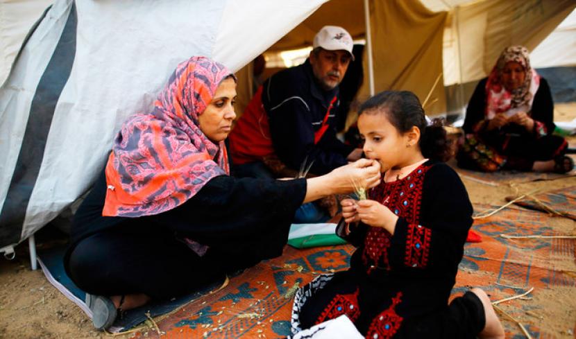 Seorang wanita Palestina menyuapkan makanan kepada putrinya di sebuah tenda dekat lokasi bentrokan antara demonstran Palestina dan pasukan Israel menyusul protes di sepanjang perbatasan dengan Israel, sebelah timur Kota Gaza, pada 3 April 2018.