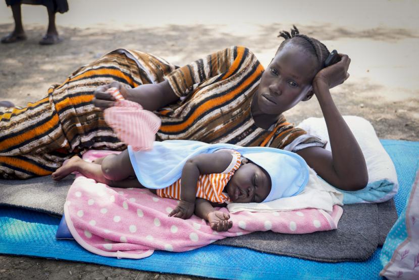 Seorang wanita Sudan Selatan yang melarikan diri dari pertempuran di Sudan terbaring di tanah dengan anaknya di bawah pohon setelah kembali ke kota Malakal, yang menampung ribuan orang yang kembali, di negara bagian Upper Nile, Sudan Selatan, Minggu, 8 Mei 2023.