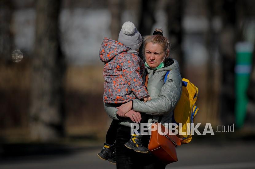  Seorang wanita Ukraina menggendong seorang anak setelah melintasi perbatasan dari Ukraina di perbatasan Rumania-Ukraina, di Siret, Rumania, Jumat, 25 Februari 2022. Duta Besar Rusia untuk PBB menyebut  warga sipil Ukraina jadi tameng manusia. 
