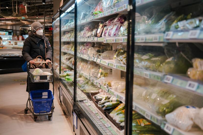 Seorang wanita yang mengenakan masker berjalan di samping area produk makanan segar di sebuah supermarket di Beijing, China, 16 Desember 2022.