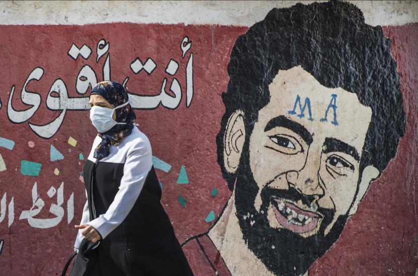 Seorang wanita yang mengenakan topeng pelindung berjalan di depan mural yang menggambarkan striker Liverpool Mesir Mohamed Salah di Kairo, Mesir. Ilustrasi.